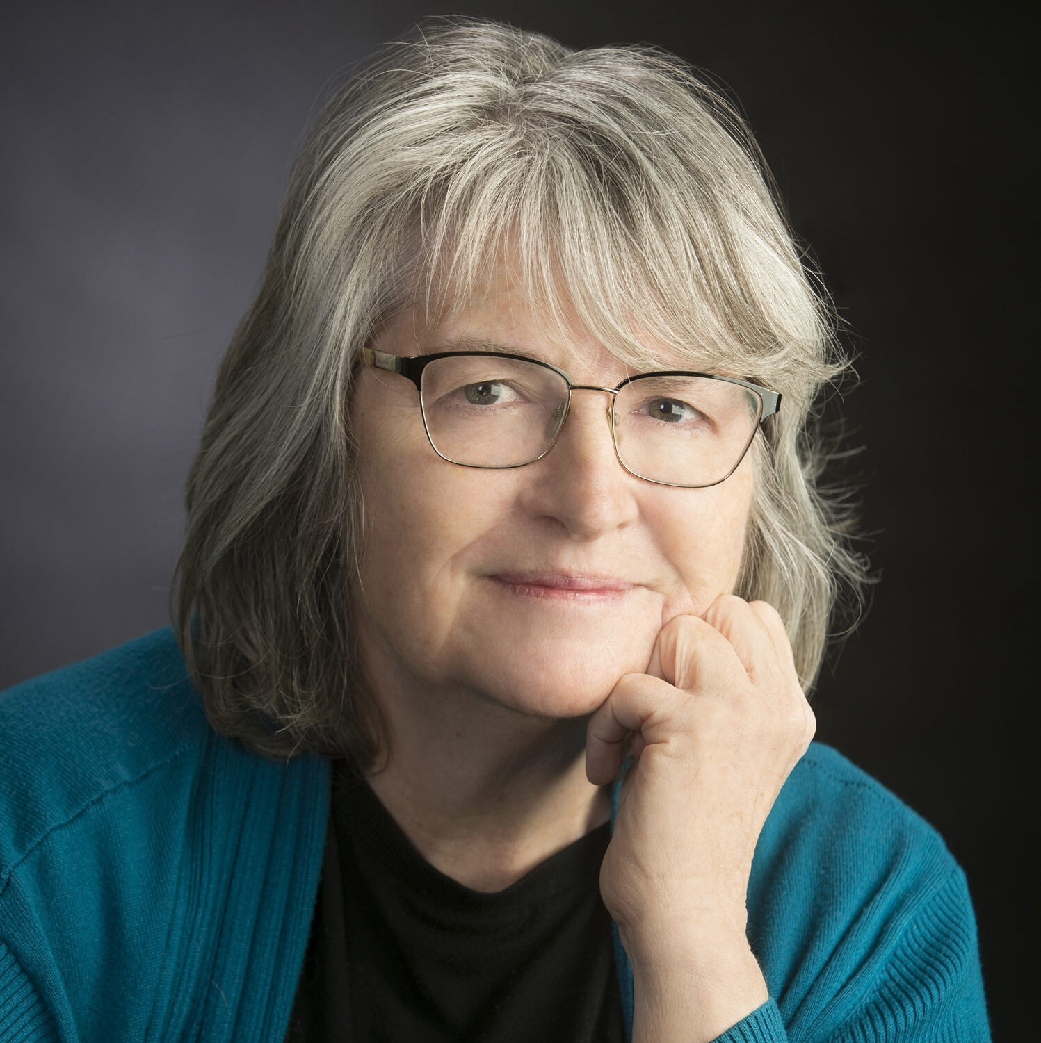 A woman wearing glasses poses with a hand on her chin
